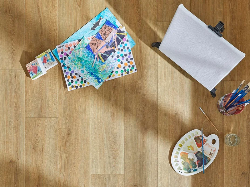 Light wood-look floors with a child’s art supplies show how durable laminate flooring is.